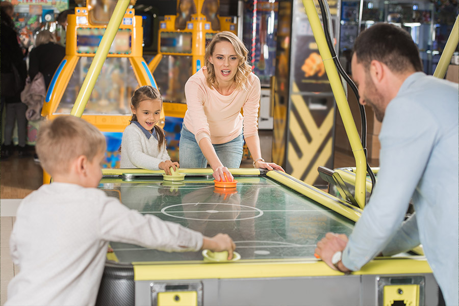 Family Entertainment Center Insurance - Family Playing Air Hockey on a Table in an Arcade While Smiling and Laughing